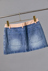 Blue denim skirt on a hanger against a gray background