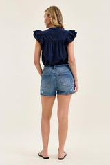 Woman wearing a navy top and denim shorts on a white background